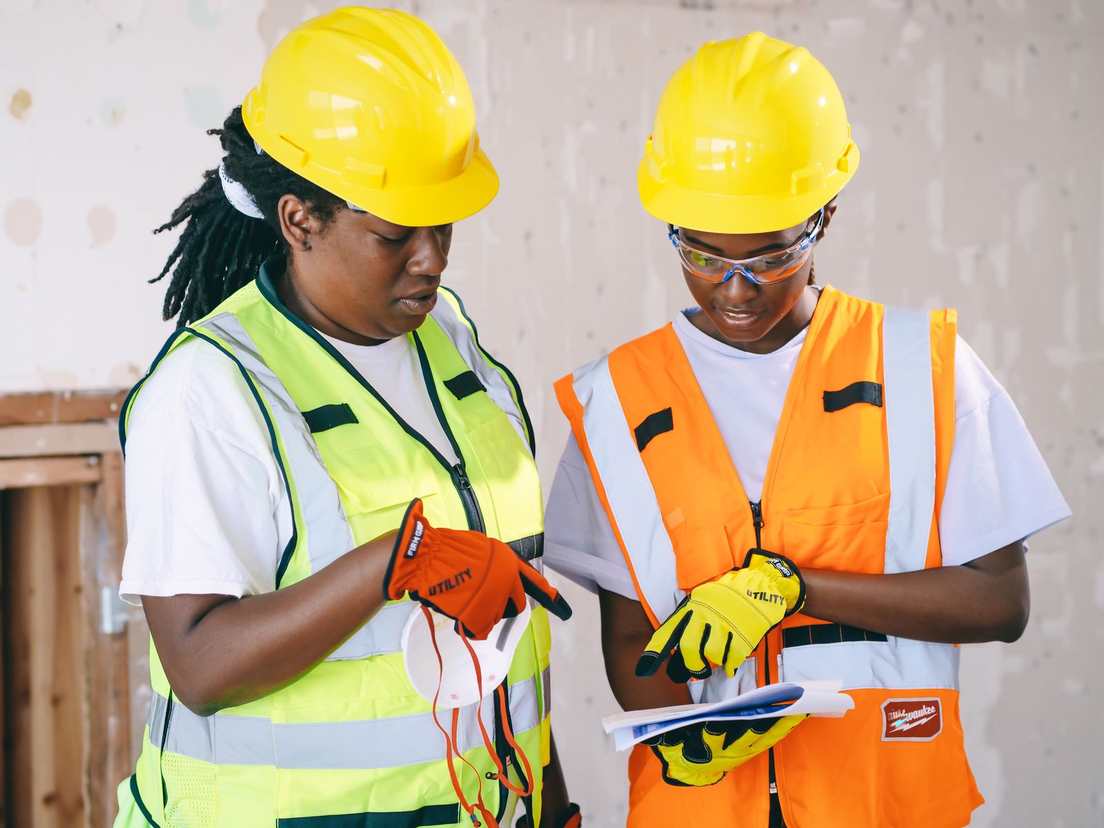 Two construction professionals in safety helmets and high-visibility vests reviewing documents